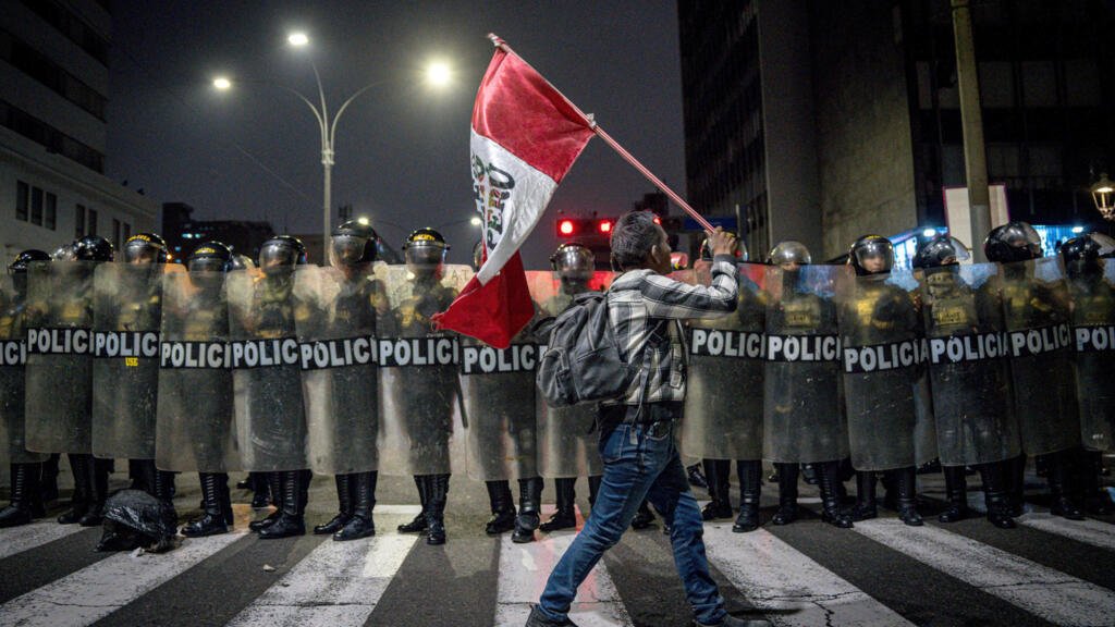 Una persona sostiene una bandera de Perú frente a integrantes de la Policía de Perú. Los jóvenes de la denominada 'Generación Z', junto a otros colectivos sociales, partidos y gremios laborales, llegaron en marcha hacia los exteriores del Parlamento el miércoles 15 de octubre.