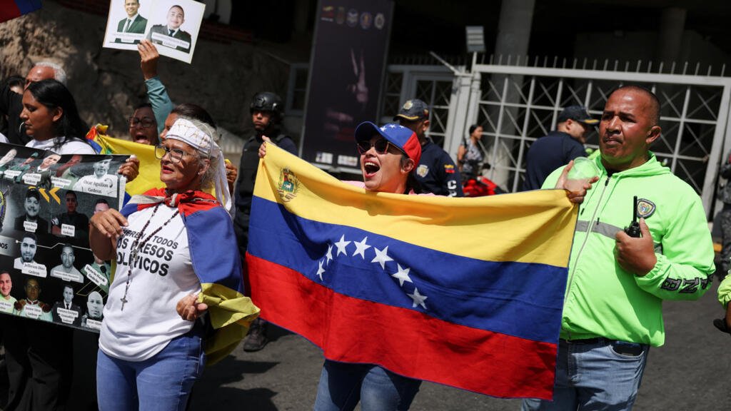 Personas sostienen banderas venezolanas, carteles y una pancarta frente a agentes del orden, mientras familiares de presos políticos protestan frente al edificio Helicoide después de reunirse para una oración en apoyo a una ley de amnistía, la liberación de presos políticos y el diálogo nacional, en Caracas, Venezuela, el 7 de febrero de 2026.